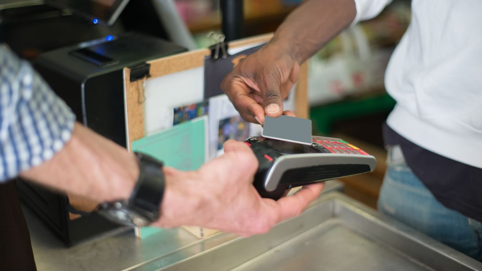 A hand tapping a card on a payment terminal at a shop counter
